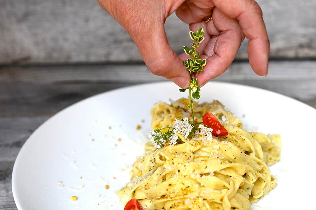 Close-up view of a hand placing garnish onto a plate of pasta.